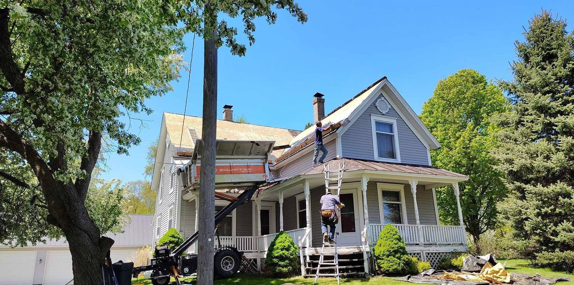 Roofing crew replacing a storm-damaged roof on a West Michigan farmhouse with exposed decking visible Roofing crew replacing a storm-damaged roof on a West Michigan farmhouse with exposed decking visible